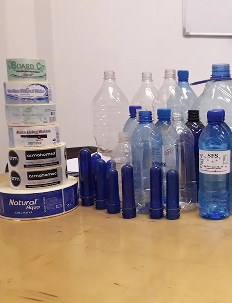 Blue preforms, caps, rolls of labels and finished PET bottles on a workbench