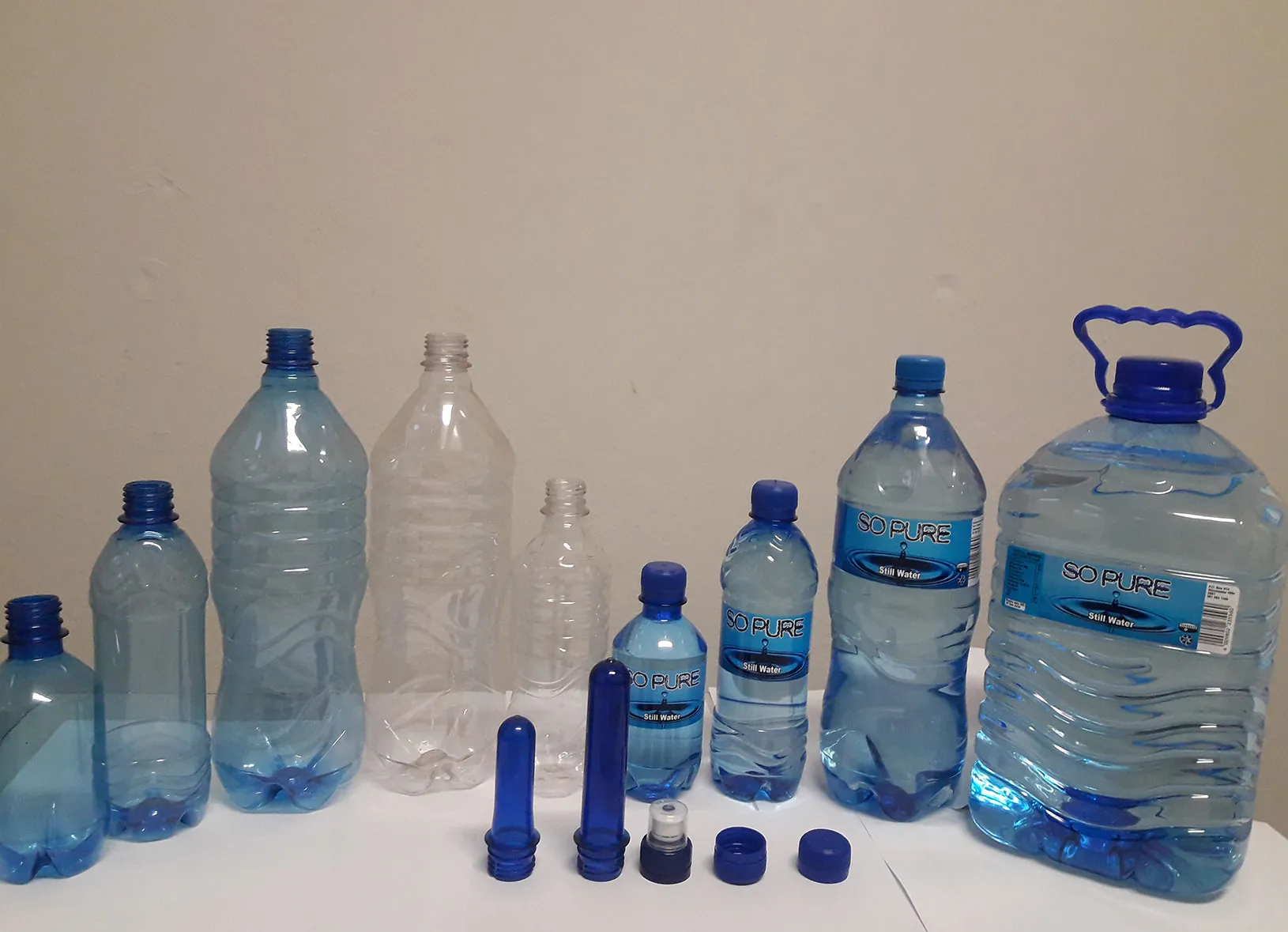 Empty clear and blue PET bottles from 330ml to 5 litres with blue preforms and caps in front